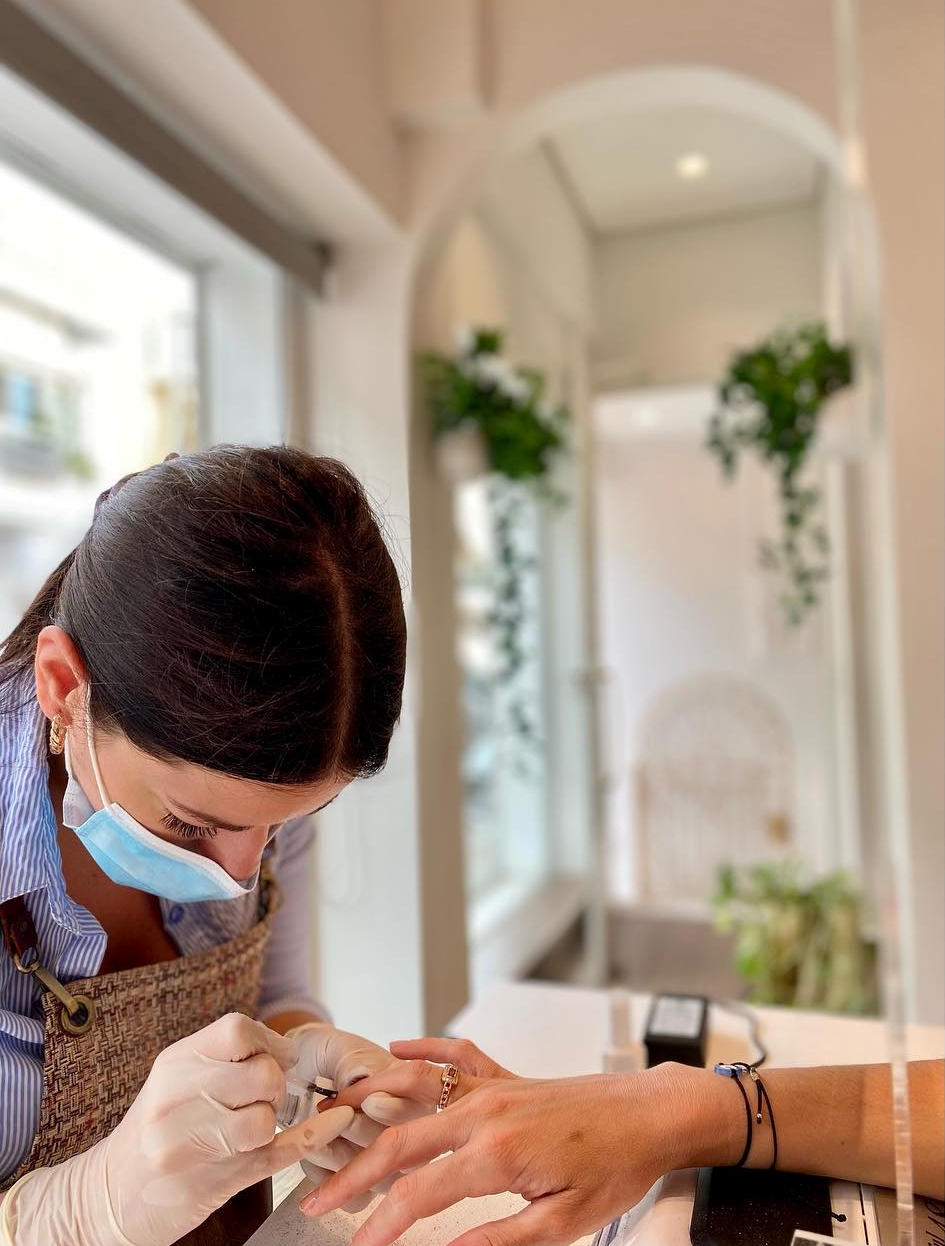 Αισθητικός του Naloo Beauty Bar εφαρμόζει ημιμόνιμο μανικιούρ σε πελάτισσα στο κατάστημα στο Περιστέρι